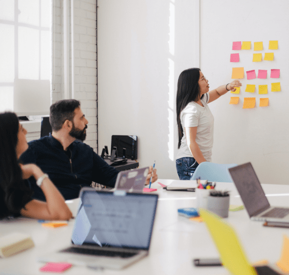 Woman pointing to sticky notes about 12 simple team building activities. Credit You X Ventures